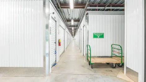 Interior of a self-storage facility showing a rolling cart in the aisle, with storage units on both sides.